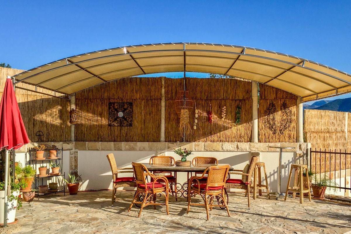 An outdoor patio with a covered seating area, stone flooring, and potted plants.
