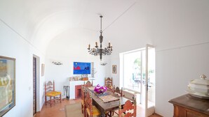 A dining room with a wooden table, chairs, a chandelier, and artwork on the walls. - Villa Le Tuie by Elite Villas (Capri)