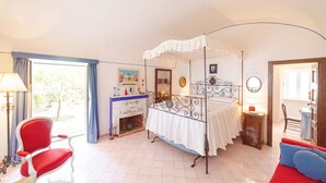 A bedroom with a four-poster bed, a red chair, a red sofa, a fireplace, and a large window. - Villa Le Tuie by Elite Villas (Capri)