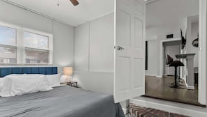 Een slaapkamer met een bed, nachtkastje, lamp en raam met zonwering.
