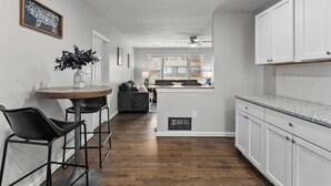 Een moderne keuken met witte kastjes, een granieten aanrechtblad en een eethoek met een ronde tafel en twee stoelen.