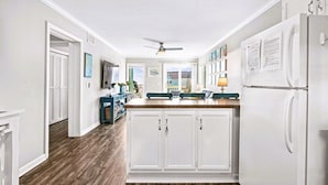 A kitchen with white cabinets, a refrigerator, a ceiling fan, and a view to the outside.