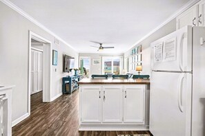 Una cocina con armarios blancos, un refrigerador, un ventilador de techo y vistas al exterior.