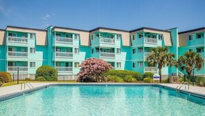 A turquoise multi-story building with balconies, a swimming pool, and palm trees.