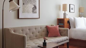 Habitación de hotel con sofá, mesita auxiliar, lámpara, cuadro enmarco y cama con almohadas.
