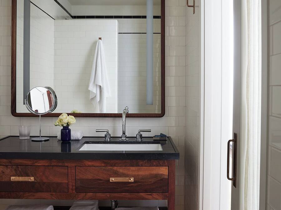 Un baño con tocador de madera, un espejo grande, un lavamanos blanco y un perchero para toallas.