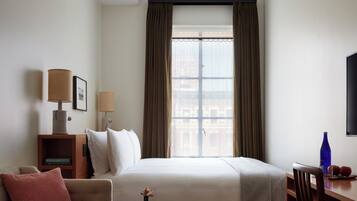 Habitación de hotel con cama, sofá, escritorio, silla, lámpara, un marco de fotos y ventana con cortinas.