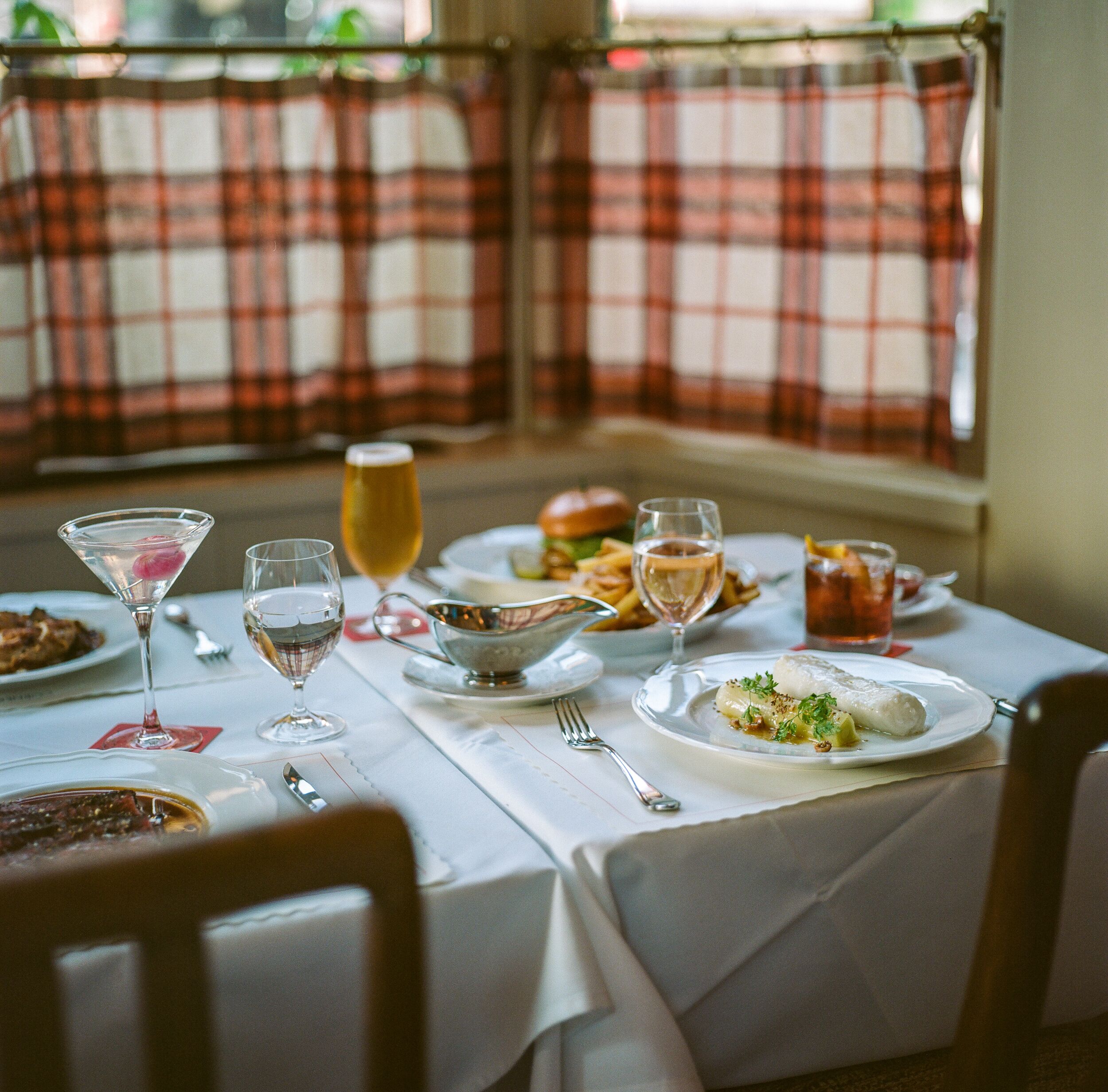 A dining table set with various dishes, glasses, and cutlery, with plaid curtains in the background.
