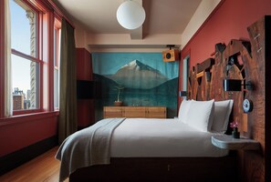 Een slaapkamer met een groot bed, een houten hoofdbord, een schilderij van een berg, een raam met gordijnen en een nachtkastje met een lamp.