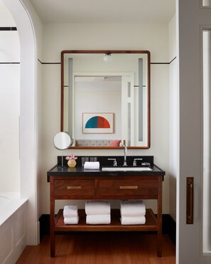 Een badkamer met een houten wastafelmeubel, een grote spiegel en een kunstwerk in een lijst erboven.