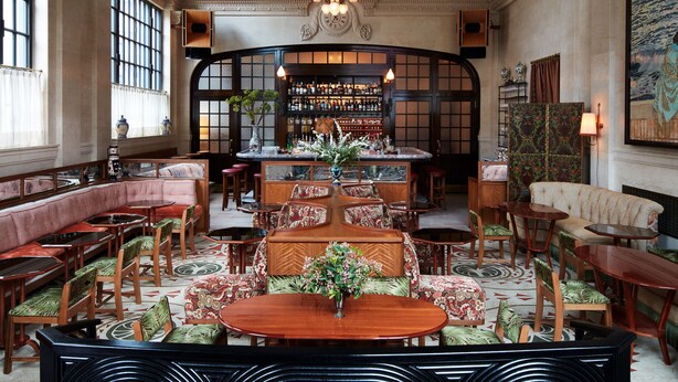 A grand lobby with a high ceiling, ornate chandeliers, and a bar area with a clock. - Nine Orchard (New York)