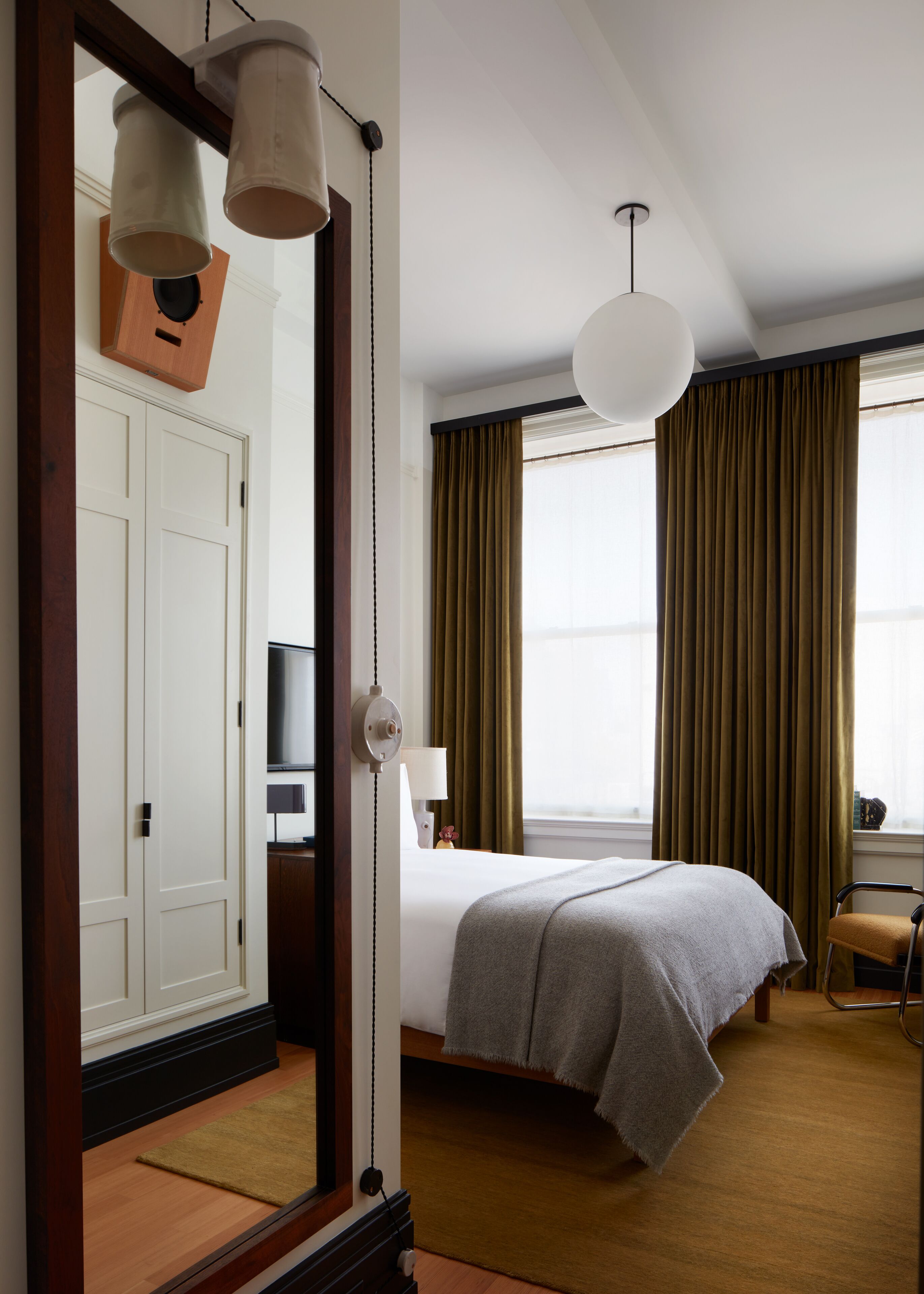 Habitación de hotel con cama, escritorio, silla, televisor y un espejo grande.