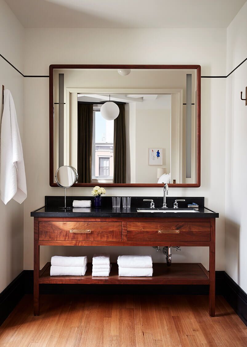 A modern bathroom with a wooden vanity, a large mirror, and a hanging light fixture.