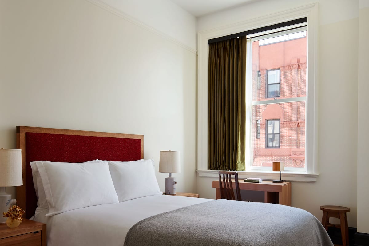 Ein ordentlich eingerichtetes Hotelzimmer mit einem großen Bett, einem Schreibtisch und einem Fenster mit Vorhängen.