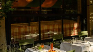 An outdoor dining area with tables and chairs, a green awning, and a view of the interior through large windows. - Nine Orchard (New York)