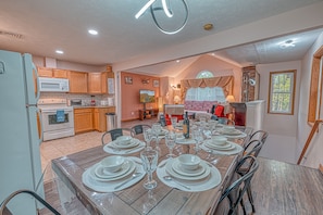 A spacious kitchen with wooden cabinets, a dining area set for six with a wooden table, and a cozy living room with a fireplace.