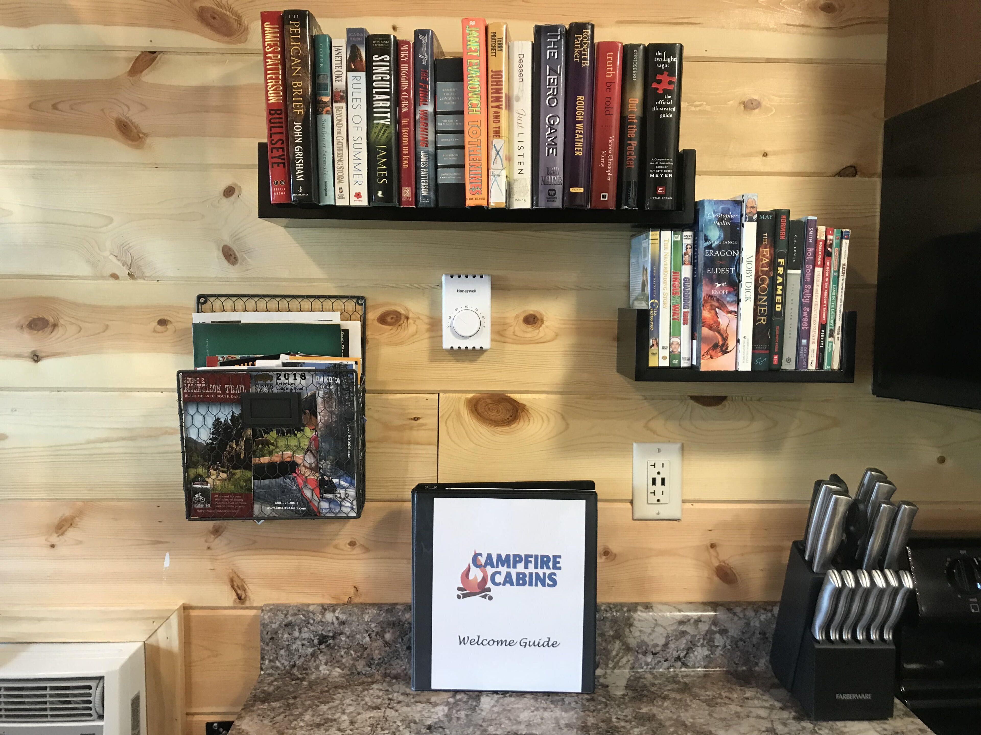 Una cocina equipada con cafetera, una estantería con varios libros, una guía de bienvenida y un bloque de cuchillos.