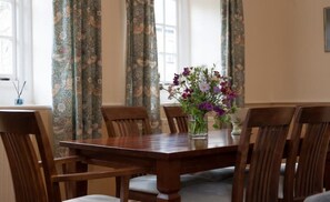 A dining room with a wooden table and chairs, floral centerpiece, and patterned curtains. - Fine period home on country estate, Lyme Regis (Lyme Regis)