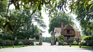 A traditional stone building with a pitched roof, surrounded by lush greenery and a paved driveway. - Fine period home on country estate, Lyme Regis (Lyme Regis)