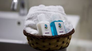 A bathroom with a white bathtub, a white towel, and a wicker basket containing two bottles of hotel shampoo.