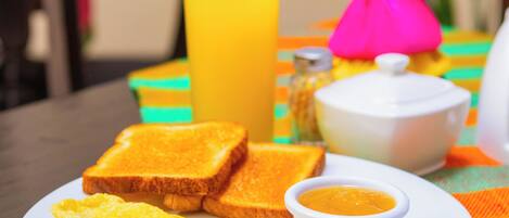 Une assiette de petit-déjeuner avec des toasts, une omelette et un petit bol de sauce, accompagnée d’un verre de jus d’orange, le tout posé sur une nappe colorée.