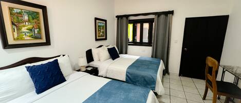 A hotel room with two beds, a desk, a chair, and two framed pictures on the wall.