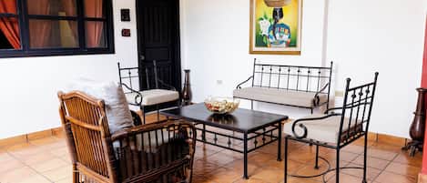 Una habitación con un sofá de mimbre, dos sillones, una mesita y una puerta negra.