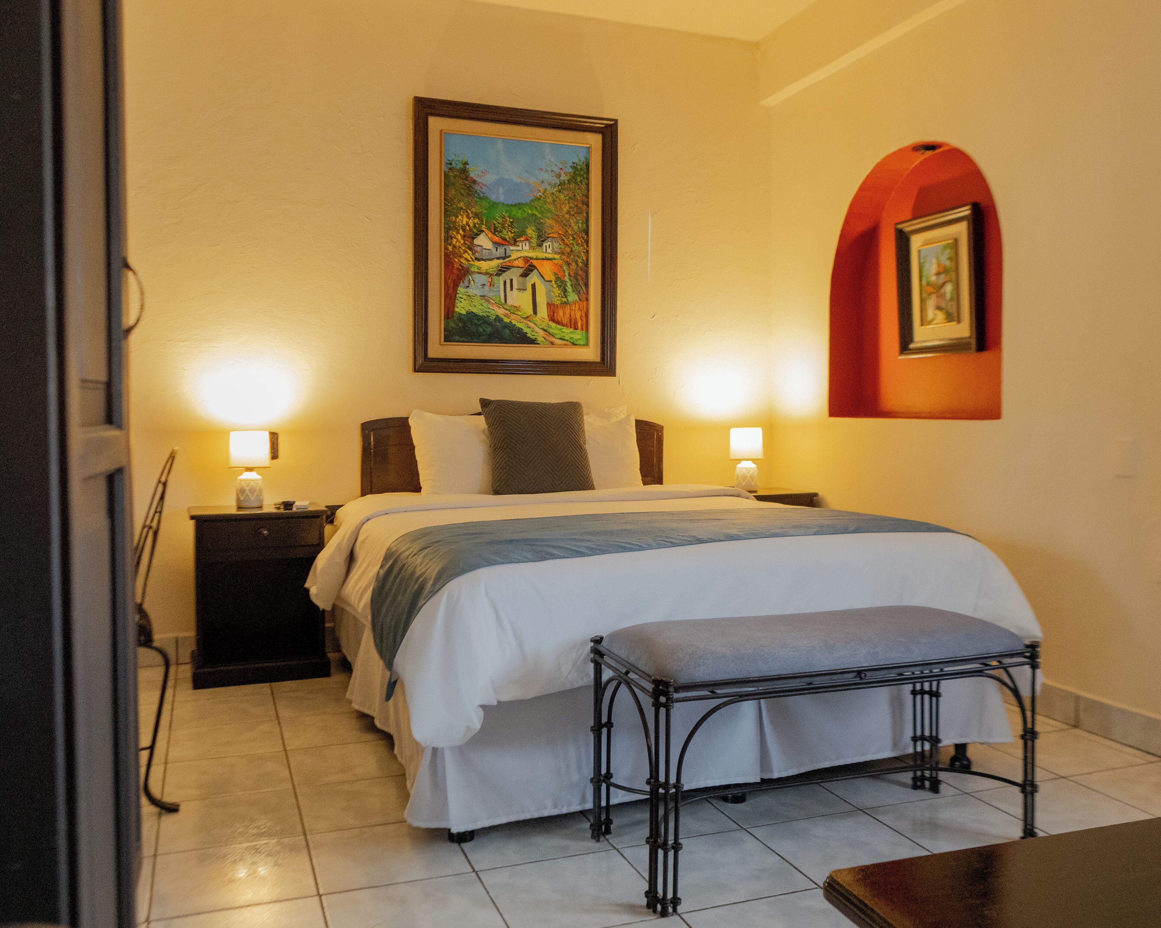 A neatly arranged bedroom with a bed, bedside tables, a bench, and two wall-mounted lamps.