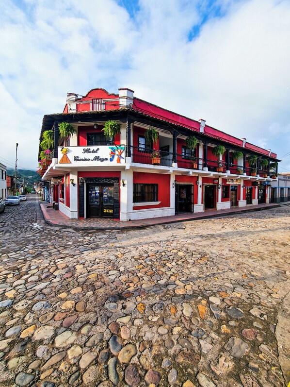 A hotel with multiple balconies, a red and white facade, and a cobblestone street in front. - Hotel Camino Maya (Copan Ruinas)