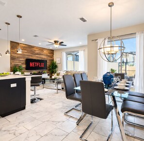 A modern dining area with a glass table, black chairs, and a ceiling fan.