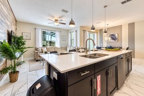 A modern kitchen with a central island, black cabinetry, stainless steel appliances, and pendant lighting.