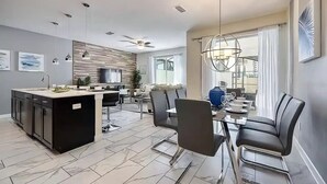 Une cuisine moderne dotée d’un îlot central, d’un coin repas avec des chaises et d’un ventilateur de plafond.