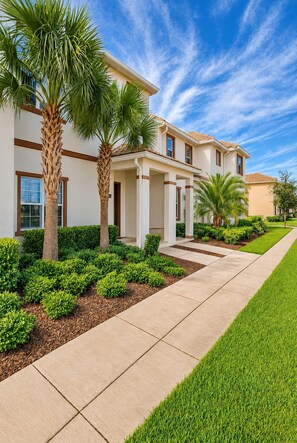 A residential building with a covered patio, palm trees, and a well-maintained lawn.