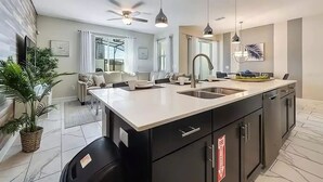 Une cuisine moderne dotée d’un grand îlot central, de meubles de couleur noire et d’un éclairage suspendu.