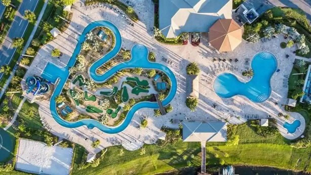 Vue aérienne d’un complexe hôtelier doté de plusieurs piscines, d’un cours d’eau sinueux et d’espaces paysagers aménagés.