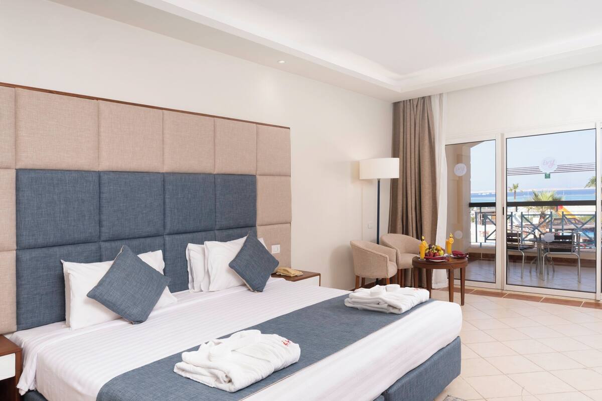 A hotel room with a large bed, a balcony with a view, a desk with a lamp, and a chair.