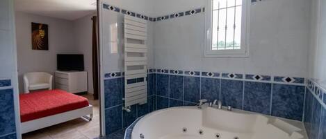 A bathroom with a large bathtub, a shower area, and a toilet. There is a window providing natural light and a towel rack above the bathtub.