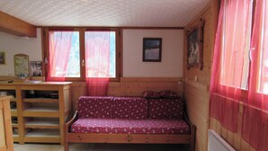 A cozy room with a wooden bed, a desk, and a window with red curtains. - Studio Aux Bossons (3km From Chamonix Mont Blanc ) (Chamonix Mont-Blanc)