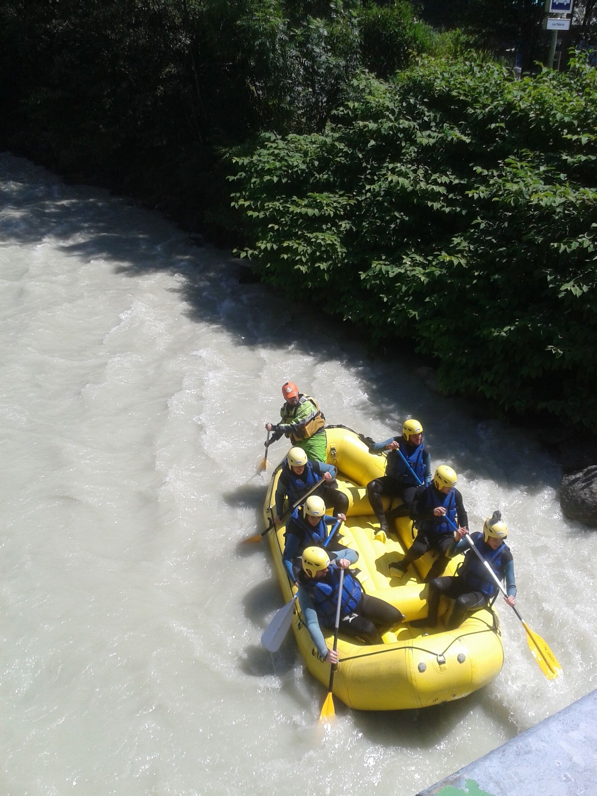 A group of people in a yellow raft navigating a river surrounded by dense greenery.