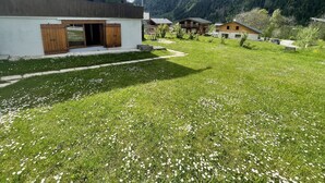 A modern house with a large grassy yard, wooden shutters, and a mountain backdrop. - Studio Aux Bossons (3km From Chamonix Mont Blanc ) (Chamonix Mont-Blanc)
