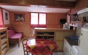 Cozy cabin kitchen with a stove, sink, and refrigerator, offering a compact dining area with a round table and wooden chair.