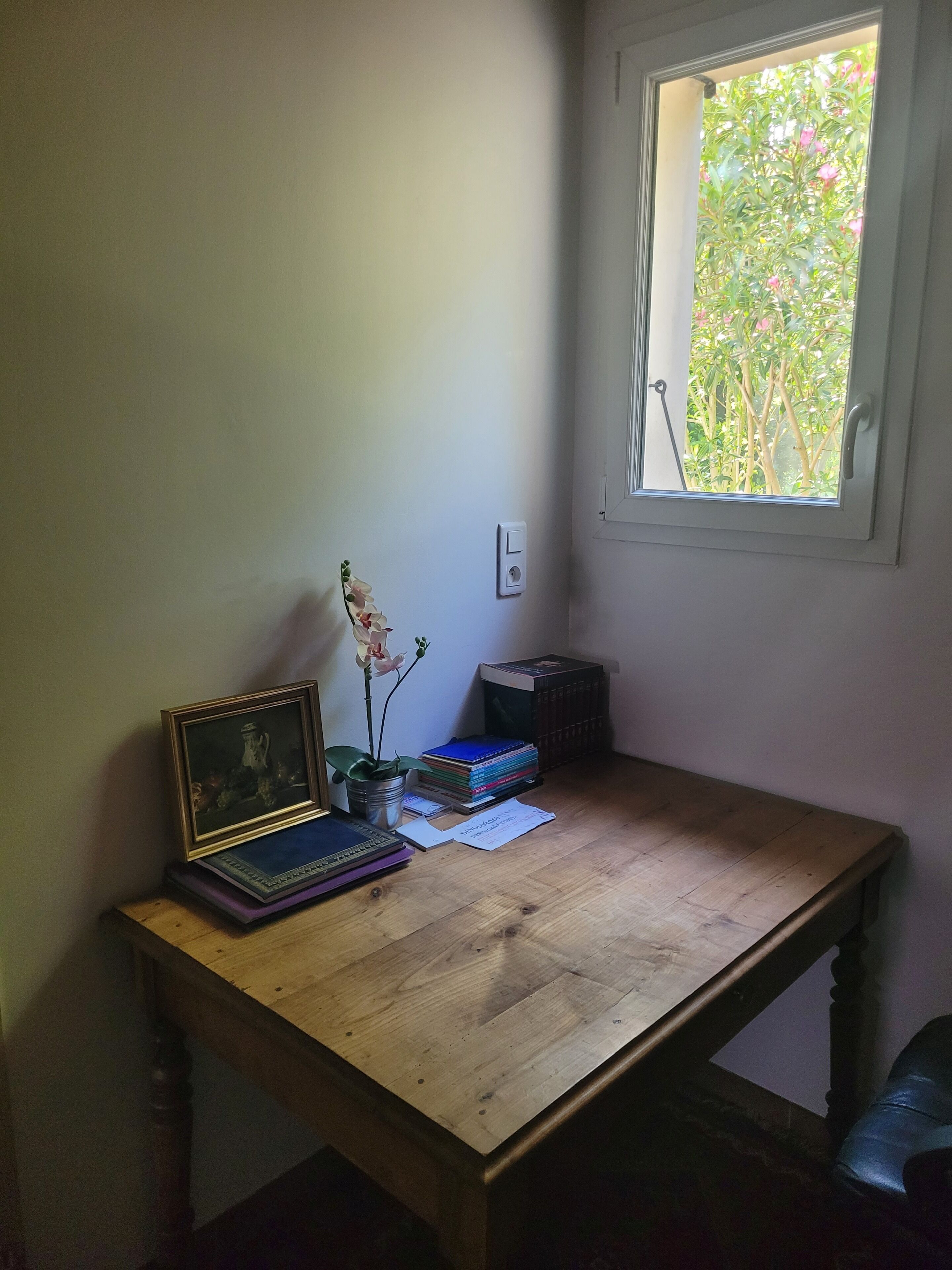 A wooden desk with a laptop, books, a vase with flowers, and a framed picture.