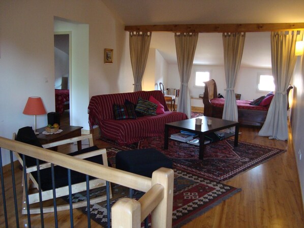 A living room with a red sofa, a wooden coffee table, and a patterned rug. There is a staircase with a wooden railing leading to an upper level.