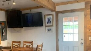 Ein Essbereich mit Holztisch und Stühlen, einem Wand-Fernseher und einer Tür mit Ausblick.