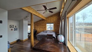 Ein geräumiges Schlafzimmer im Loft-Stil mit schrägem Dach, Holzbalken, einem großen Bett, einem Schreibtisch und einem Globus.