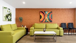Een woonkamer met twee groene banken, een witte salontafel en twee zwarte stoelen.