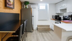 Een moderne keuken met een eethoek, met een houten eettafel, zwarte stoelen, een koelkast, een magnetron en een koffieapparaat.