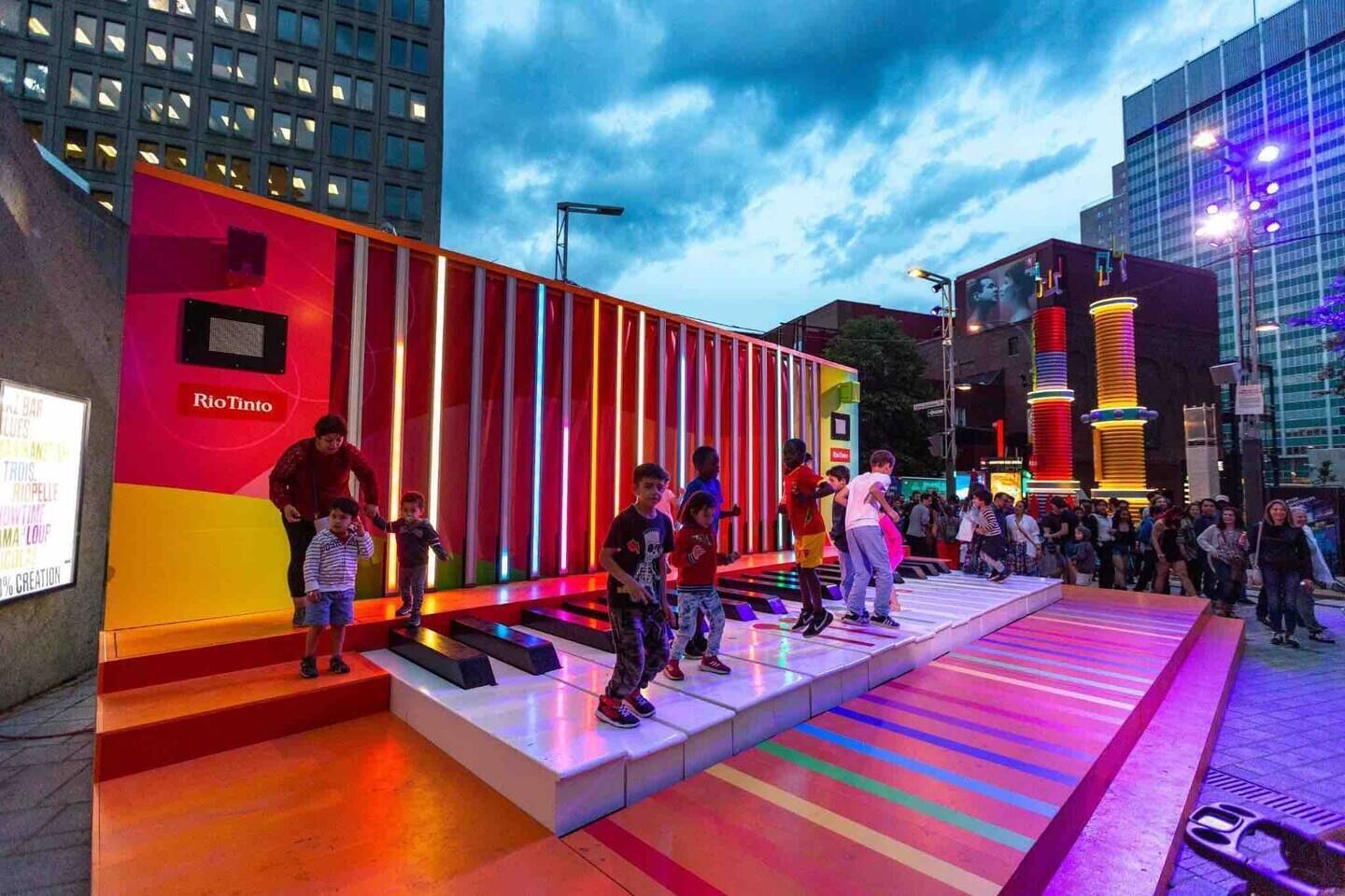 An outdoor urban space with a colorful, illuminated structure and steps leading up to it.