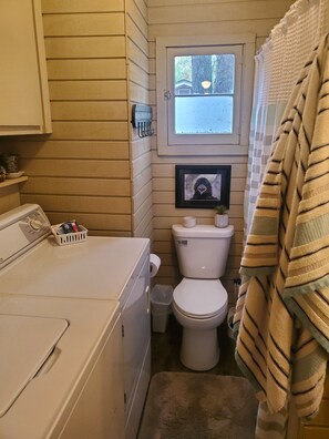 A compact bathroom with a window, a toilet, a washing machine, and a towel rack. - Quaint Cottage near Cranberry Lake (Harrison)