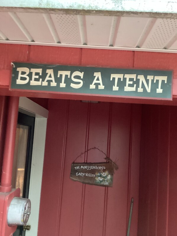 A red building with a sign that reads "BEATS A TENT" and another sign below it that says "THE MOEGGENBERG'S GARY KELLY". - Quaint Cottage near Cranberry Lake (Harrison)